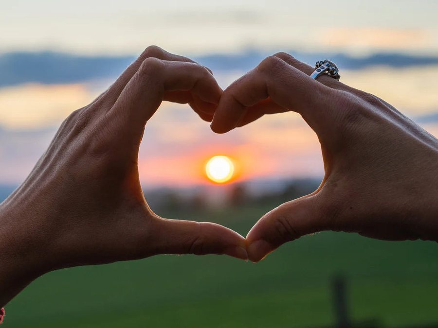 Two hands forming a heart around the setting sun