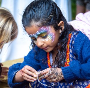 A girl with face paint making a garland